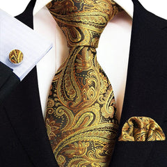 A black suit worn with a gold and black paisley necktie, matching pocket square, and cufflinks.