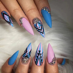 Long stiletto press-on nails featuring blue and pink stripes, geometric patterns, and rhinestones.