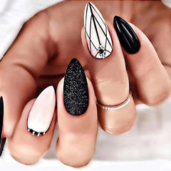 A hand displays almond-shaped press-on nails featuring black and white geometric and glitter designs.