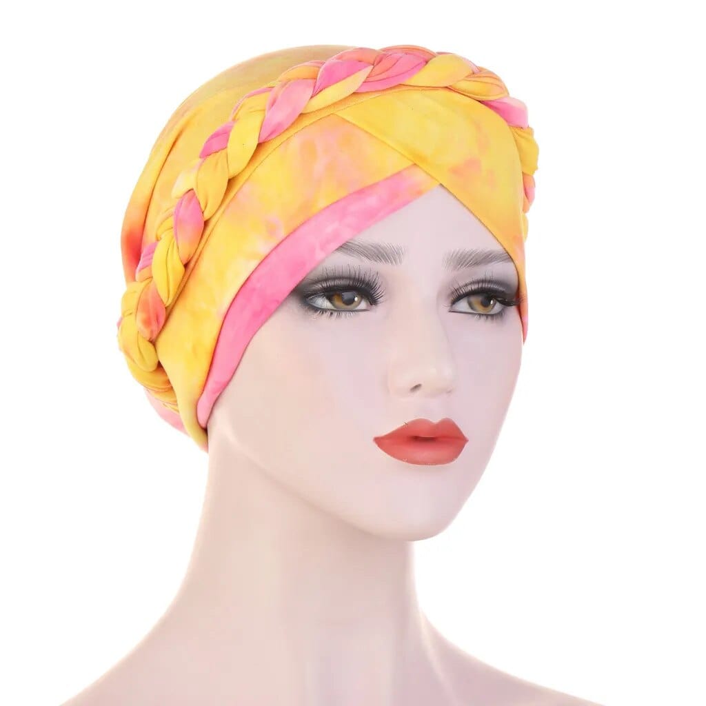 A mannequin wears a yellow and pink tie-dye turban with a braided headband detail.