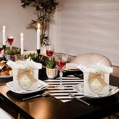 Two white mini gift bags with Thank You text and gold bows sit on a decorated dining table.