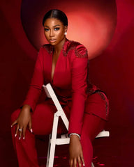 A woman wears a red two-piece suit featuring a V-neck jacket with beaded shoulder embellishments.