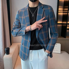 A man wears a blue plaid single-breasted blazer with a notched lapel over a black t-shirt.