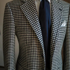 A men's black and white houndstooth blazer featuring a notched lapel and single-breasted closure.
