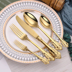 A set of four gold-colored stainless steel utensils with ornate relief handles on a patterned plate.