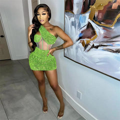 A woman wears a lime green, one-shoulder mini dress featuring sequins and sheer mesh panels.