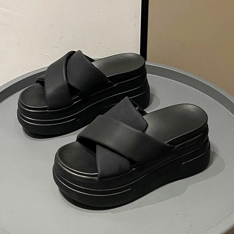 A pair of black platform slide sandals with thick crisscross straps on a chunky muffin sole.