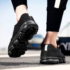 A pair of black breathable mesh sneakers with thick shock-absorbing soles worn by a person.