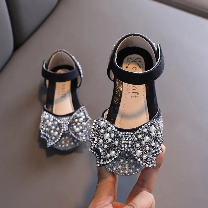 Girls' flat leather princess sandals with sequins and bow detail, perfect for summer parties and special occasions.