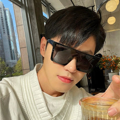 A man wears oversized black one-piece square sunglasses with a sleek, modern design.