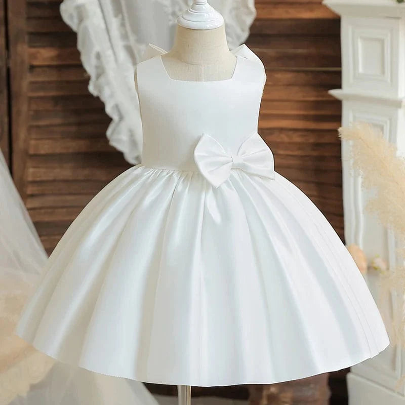 Toddler girl in a white baptism dress with a large bow, princess-style gown for special occasions like birthdays and weddings.