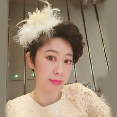 A woman wears a vintage white bridal side clip featuring a decorative flower, feathers, and netting.
