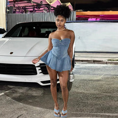 A woman wears a strapless blue denim mini dress with a corset-style bodice and a ruffled skirt.